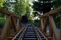 Nízký pohled na trať na dřevěném mostě. Dřevěné kolíky opravdu most drží pohromadě. Most není lepený, aby se vlivem povětrnostních vlivů nerozlepil. Před mostem naše jediná elektrická lokomotiva z produkce firmy LGB. Lokomotiva není (zatím) digitalizována, pořídili jsme ji jako nutnou součást celé startovací sady.