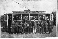 Motorový vůz ze série evid. č. 21—25 se zaměstnanci. Na snímku vidíme ženy – evidentně jde o válečné období, kdy k elektrickým drahám nastupovaly první ženy do profese průvodčí. Důvodem skupinové fotografie bude s největší pravděpodobností ukončení kursu. Motorový vůz má již upravené vstupy, boční sloupky jsou však původní. Snímek byl pořízen pravděpodobně v letech 1915—17. Autor neznámý.