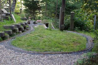 Celkový pohled na východní část kolejiště. Na snímku travnatá plocha je již aktuálně pokryta štěrkem Kačírek z důvodů minimalizace nutné údržby během vegetačního období (tráva se na kolejišti seká jen velmi obtížně). V pozadí, v nádraží Slívovice, obě naše parní lokomotivy z produkce německé firmy REGNER. Vpravo možno vidět výhybku připravenou pro vybudování roztápěcí koleje, kde by mělo být možno roztápět parní lokomotivy, aniž by se člověk musel plazit po zemi.