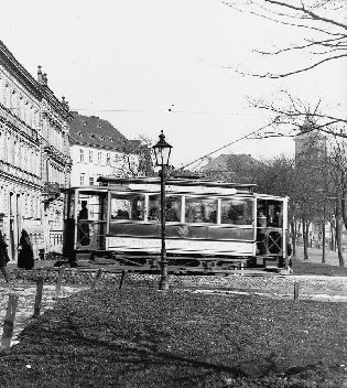 Motorový vůz série evid. č. 1—20 jedoucí na lince NÁDRAŽÍ – NÁMĚSTÍ projíždí Šafaříkovy sady do Zbrojnické ulice směrem k náměstí. Vůz je plně obsazen (místa k sezení v oddílu), stojící osoby jsou jen na zadní (nástupní) plošině. Prostor u řidiče je zcela volný. Snímek byl pořízen v letech 1900—1903. Autor neznámý. Negativ formátu 11,9 × 16,6 cm, sbírky ZČM, sign. NMP 3215. Výřez