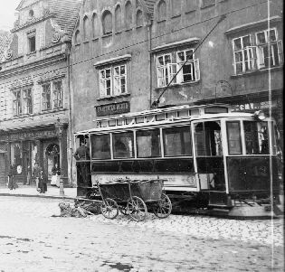Motorový vůz evid. č. 12 na náměstí. Zajímavý snímek, který dokládá původní provedení střešní pochůzné lávky. Zároveň jde již o druhý snímek tohoto vozu, kdy není namontován boční znak města. To svádí k doměnce, že z nějakého důvodu vůz evid. č. 12 znak vůbec neměl. Za povšimnutí jistě stojí vedle tramvaje odpočívající psí spřežení s károu. Jde pravděpodobně o dopravní prostředek mlékaře nebo řezníka. Snímek byl pořízen kolem roku 1900. Skleněný negativ 11,7 × 16,5 cm, sbírky ZČM, sig. NMP 609. Výřez.